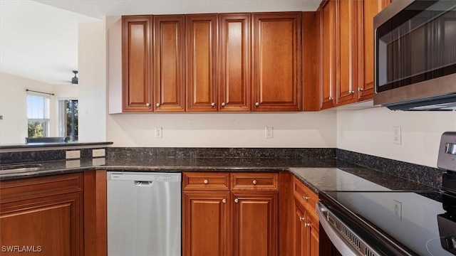 kitchen featuring dark stone countertops, stainless steel appliances, and brown cabinetry