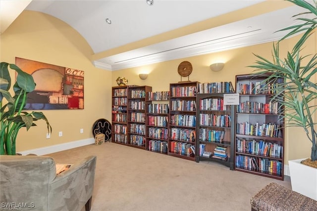 sitting room featuring wall of books, baseboards, vaulted ceiling, and carpet flooring