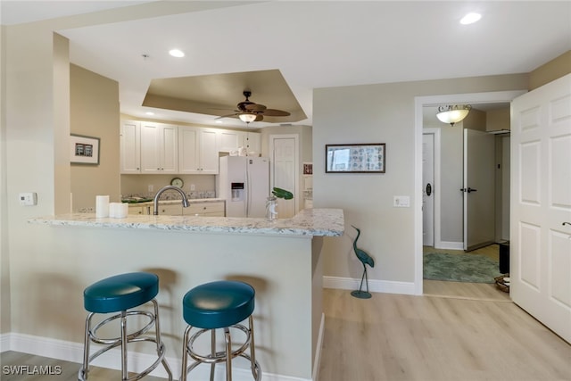 kitchen featuring a breakfast bar area, a peninsula, white cabinetry, light wood-style floors, and white fridge with ice dispenser