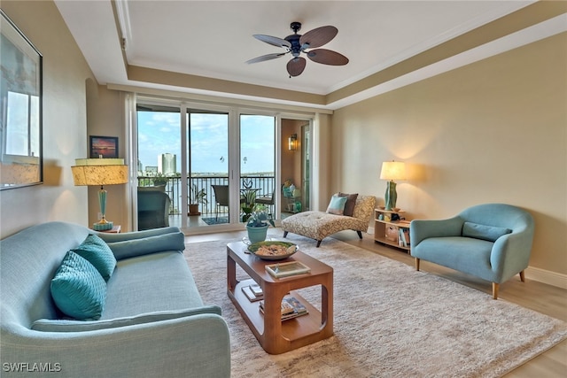 living area with a ceiling fan, baseboards, wood finished floors, and ornamental molding