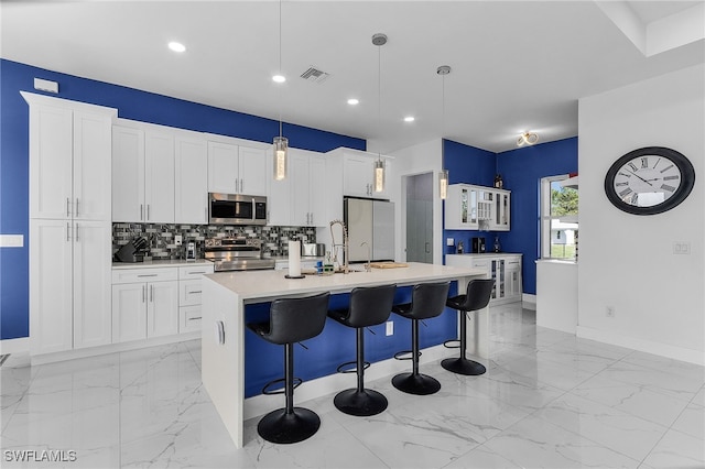 kitchen featuring a breakfast bar, an island with sink, appliances with stainless steel finishes, marble finish floor, and backsplash