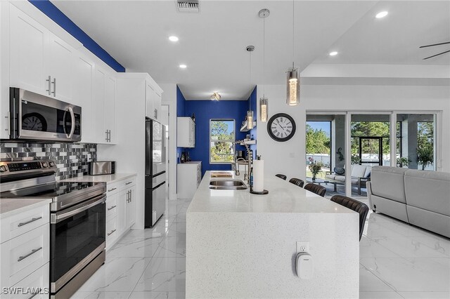 kitchen featuring open floor plan, decorative backsplash, appliances with stainless steel finishes, marble finish floor, and a sink