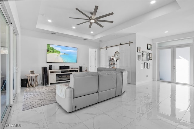 living room featuring ceiling fan, a barn door, french doors, and a tray ceiling