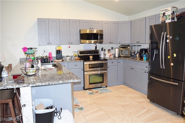 kitchen with kitchen peninsula, a kitchen bar, stainless steel appliances, sink, and stone countertops