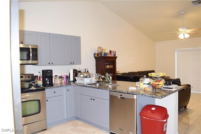 kitchen with lofted ceiling, sink, stainless steel appliances, kitchen peninsula, and dark stone counters