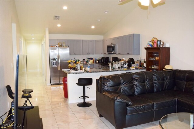 kitchen featuring lofted ceiling, gray cabinetry, dark stone countertops, a kitchen breakfast bar, and stainless steel appliances