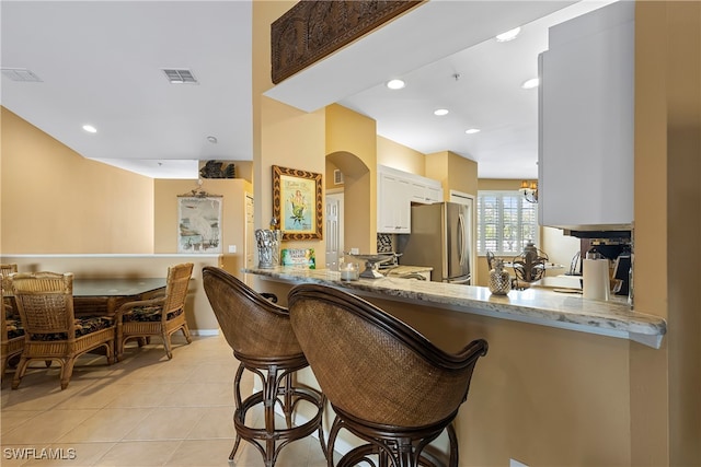 bar with stainless steel fridge, light stone counters, light tile patterned floors, an inviting chandelier, and white cabinetry