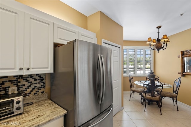 kitchen with pendant lighting, white cabinets, tasteful backsplash, stainless steel refrigerator, and a chandelier