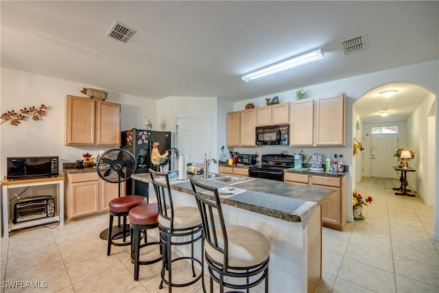 kitchen with light brown cabinetry, a breakfast bar, sink, black appliances, and a center island with sink