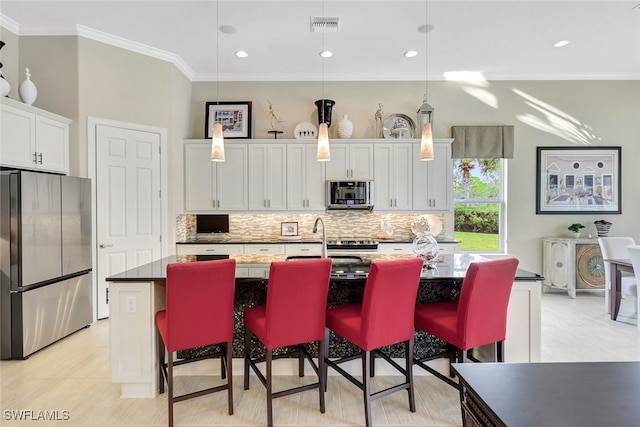 kitchen with a center island with sink, hanging light fixtures, white cabinetry, a breakfast bar area, and stainless steel refrigerator