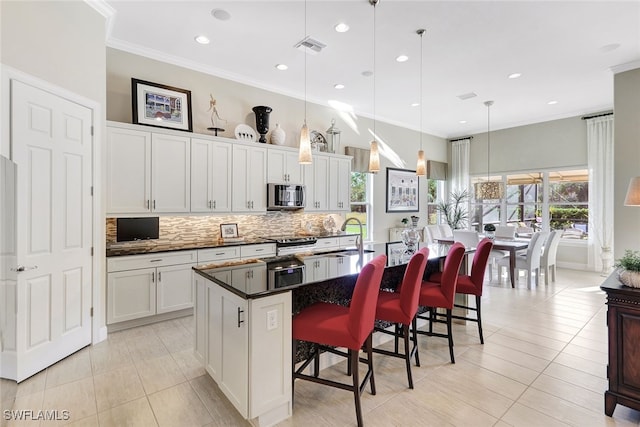 kitchen featuring white cabinets, decorative light fixtures, a kitchen bar, and a kitchen island with sink