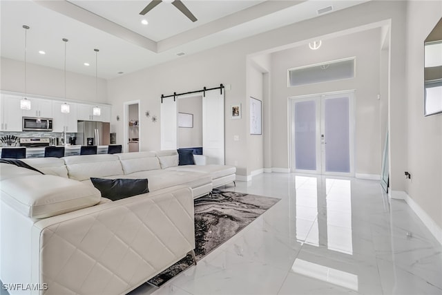 living area featuring ceiling fan, baseboards, a barn door, french doors, and a high ceiling