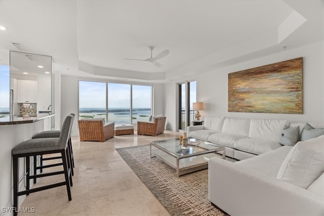 living room with a tray ceiling, ceiling fan, and a water view