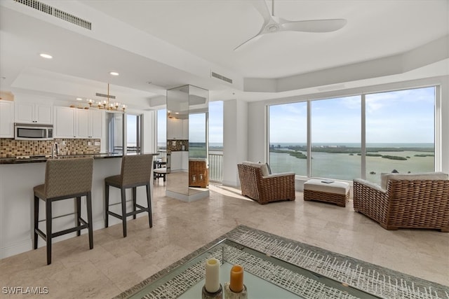 living room featuring a water view, a healthy amount of sunlight, and ceiling fan with notable chandelier