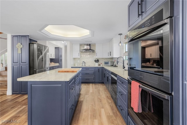 kitchen with wall chimney exhaust hood, a center island, stainless steel appliances, and light hardwood / wood-style flooring