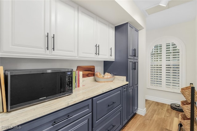 kitchen with white cabinets, light hardwood / wood-style flooring, and light stone countertops