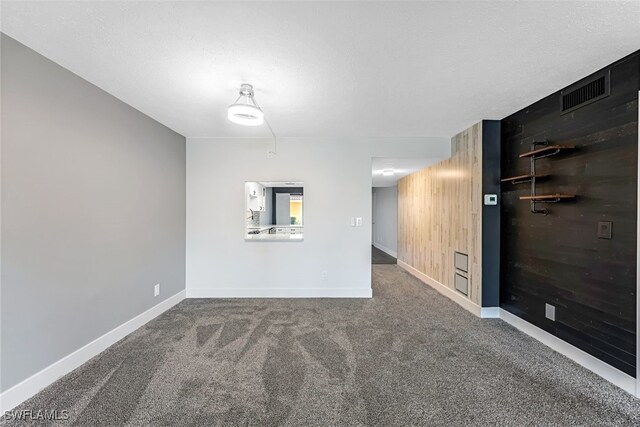 carpeted empty room with wooden walls, a textured ceiling, baseboards, and visible vents