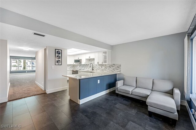 kitchen with visible vents, a sink, backsplash, white cabinetry, and a peninsula