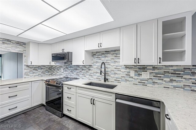 kitchen with a sink, backsplash, white cabinetry, stainless steel appliances, and light stone countertops