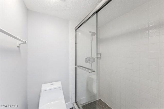 bathroom featuring toilet, a stall shower, and a textured ceiling