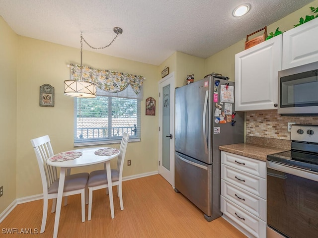 kitchen with pendant lighting, light hardwood / wood-style floors, white cabinetry, and stainless steel appliances