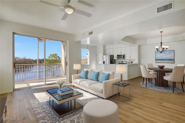 living room with ceiling fan with notable chandelier, light wood-type flooring, and a water view