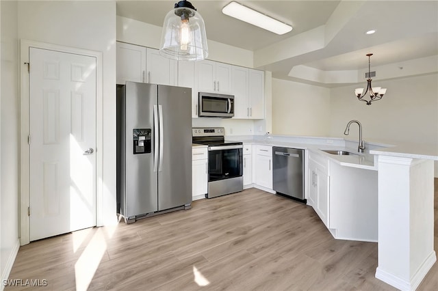 kitchen featuring kitchen peninsula, appliances with stainless steel finishes, decorative light fixtures, light hardwood / wood-style floors, and white cabinetry