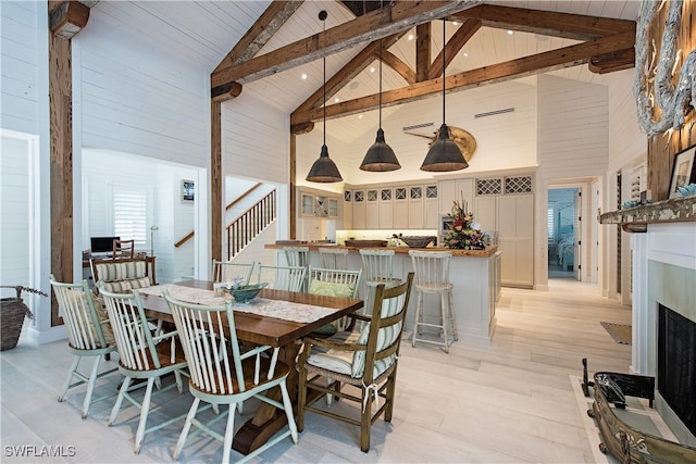 dining area with beamed ceiling, high vaulted ceiling, and light hardwood / wood-style flooring