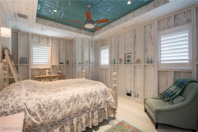 bedroom featuring multiple windows, light hardwood / wood-style flooring, ceiling fan, and wood walls