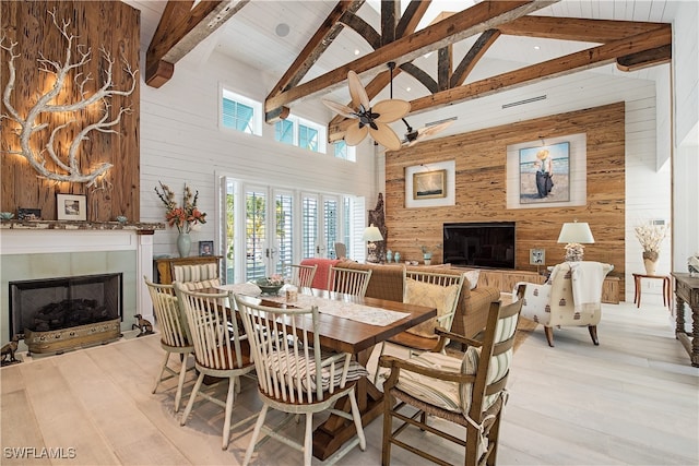 dining area with beam ceiling, wood walls, high vaulted ceiling, and light hardwood / wood-style floors