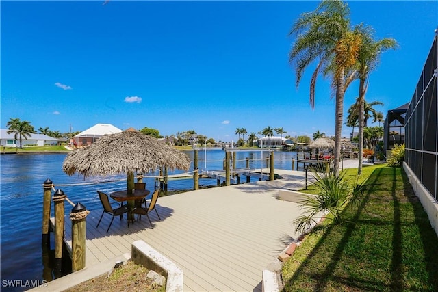 view of dock with glass enclosure, a lawn, and a water view