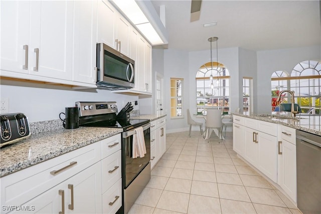 kitchen featuring light tile patterned floors, white cabinetry, appliances with stainless steel finishes, pendant lighting, and light stone counters