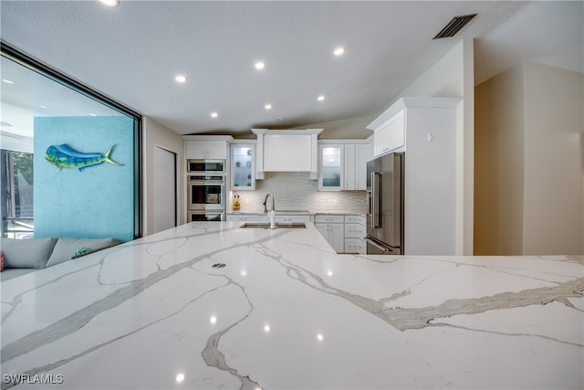 kitchen with backsplash, white cabinets, sink, light stone countertops, and stainless steel appliances