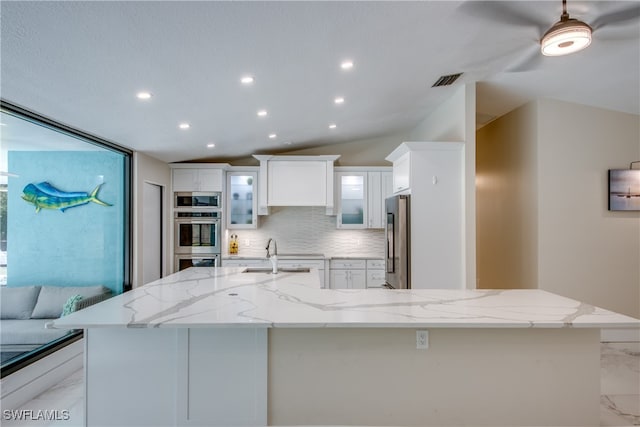 kitchen featuring a spacious island, light stone counters, stainless steel appliances, and lofted ceiling