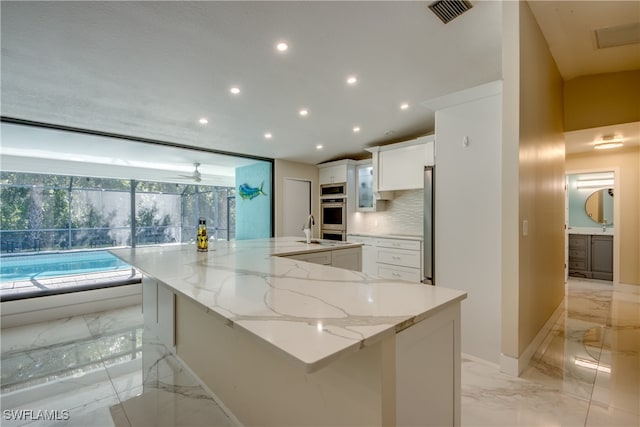 kitchen featuring decorative backsplash, light stone counters, ceiling fan, a spacious island, and white cabinetry