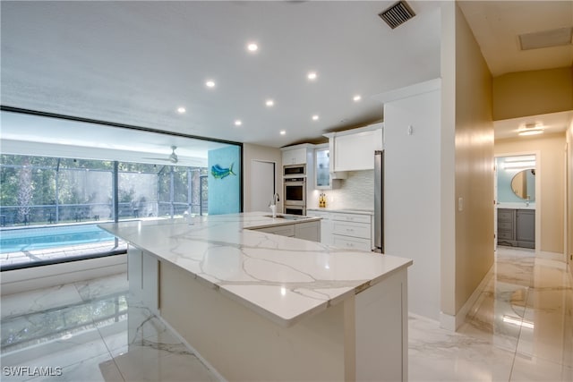 kitchen featuring white cabinetry, sink, a large island, tasteful backsplash, and light stone counters