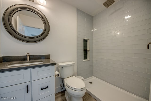 bathroom featuring hardwood / wood-style floors, vanity, toilet, and tiled shower