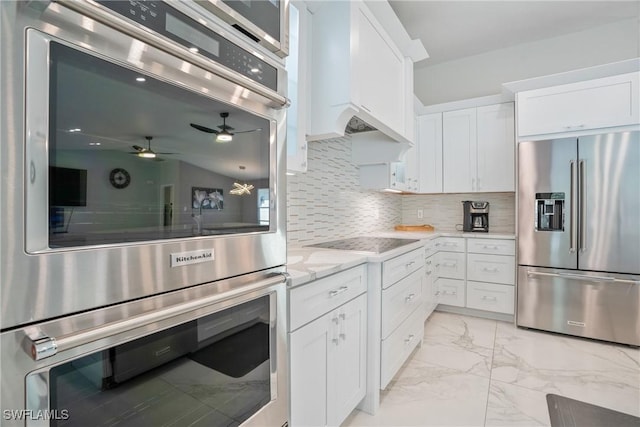 kitchen with wall chimney exhaust hood, tasteful backsplash, light stone counters, stainless steel appliances, and white cabinets