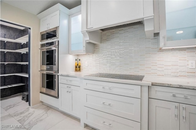 kitchen featuring cooktop, double oven, light stone countertops, decorative backsplash, and white cabinets