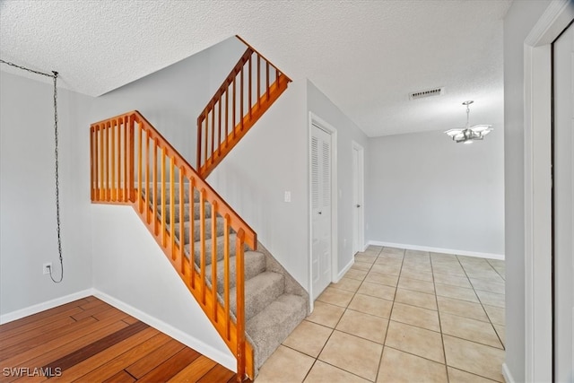 stairway featuring hardwood / wood-style floors, a textured ceiling, and an inviting chandelier