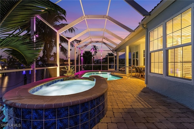 pool at dusk featuring a lanai, an in ground hot tub, and a patio