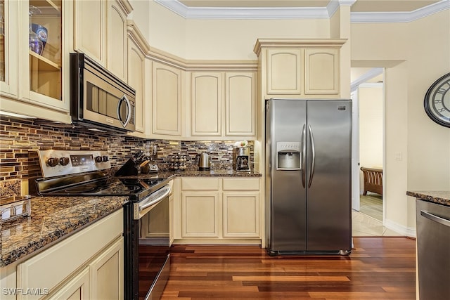 kitchen featuring cream cabinetry, dark stone countertops, dark wood-type flooring, and appliances with stainless steel finishes