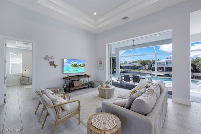 living room featuring a raised ceiling, light tile patterned floors, a healthy amount of sunlight, and ornamental molding