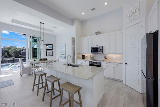 kitchen with stainless steel appliances, sink, decorative light fixtures, white cabinetry, and an island with sink