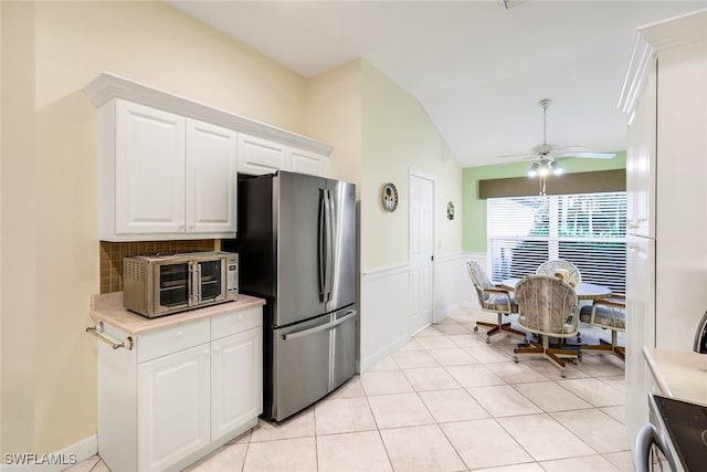 kitchen with ceiling fan, stainless steel appliances, light tile patterned floors, lofted ceiling, and white cabinets