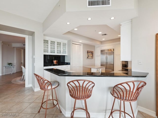 kitchen featuring kitchen peninsula, a breakfast bar, light tile patterned floors, white cabinetry, and built in fridge