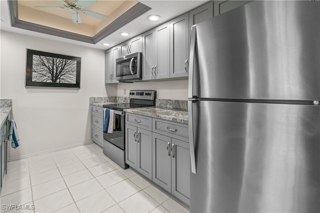 kitchen with light stone countertops, appliances with stainless steel finishes, a tray ceiling, and gray cabinetry