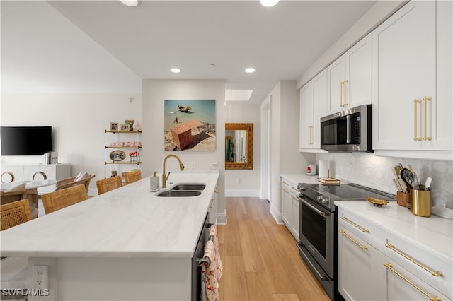 kitchen with decorative backsplash, appliances with stainless steel finishes, light wood-type flooring, sink, and white cabinets