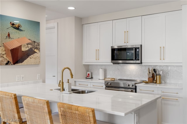 kitchen featuring white cabinetry, sink, stainless steel appliances, a kitchen breakfast bar, and light stone counters