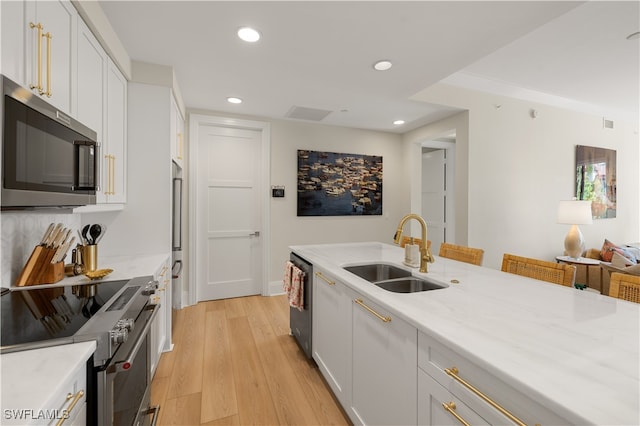 kitchen with appliances with stainless steel finishes, light hardwood / wood-style floors, white cabinetry, and sink